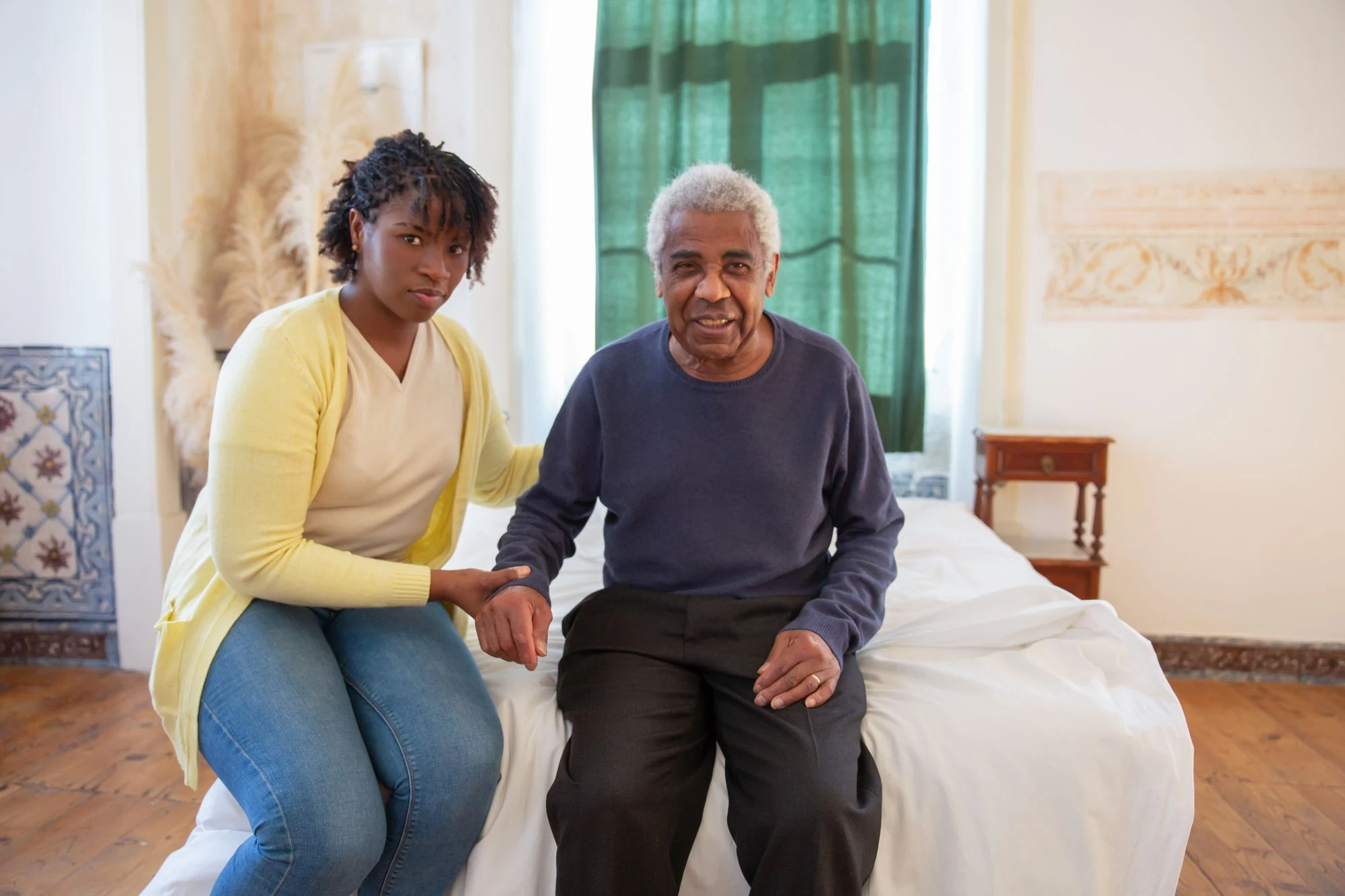 An older man sitting with a supportive companion at home.