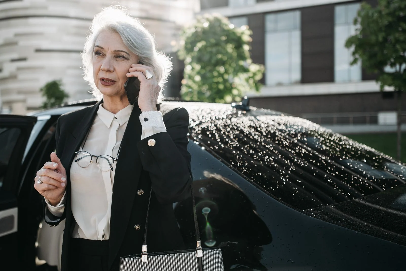 An older woman standing beside a car and using her phone.