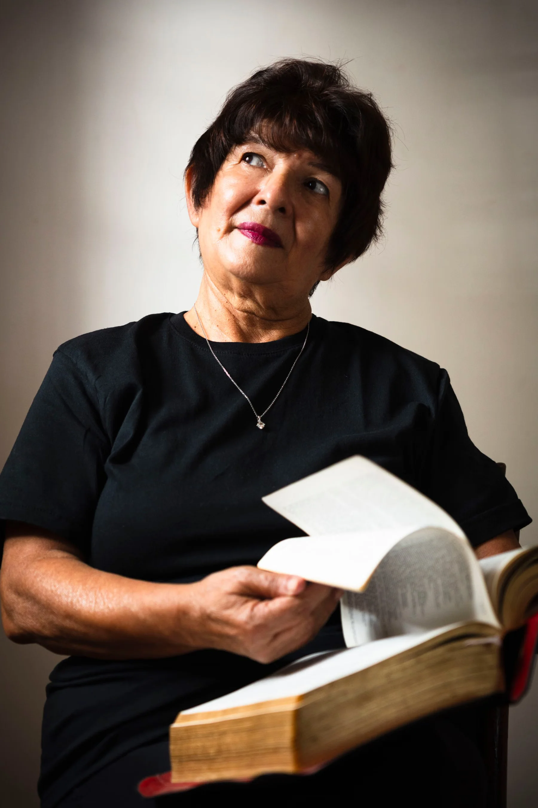 An older woman sitting with an open book.