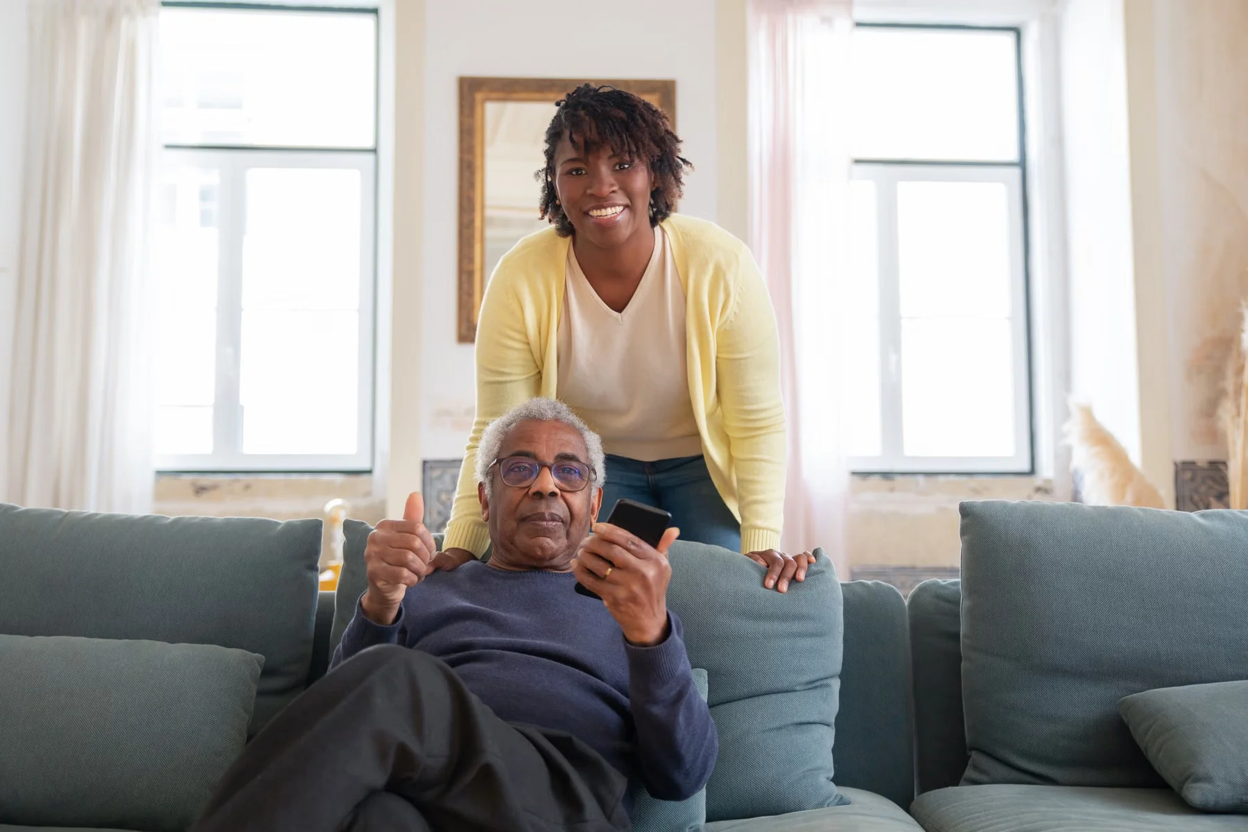 An older man relaxing on a sofa with a caregiver nearby.
