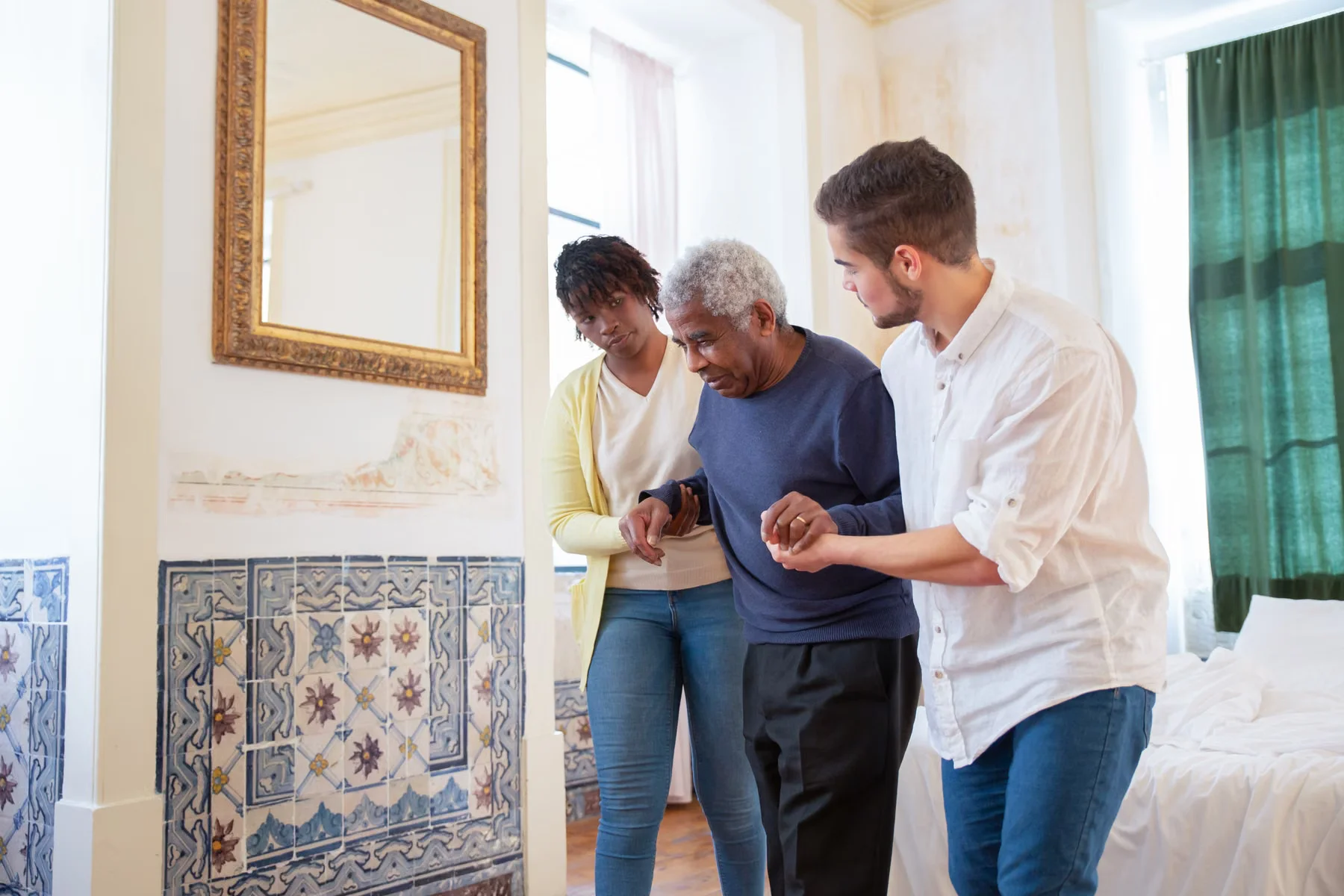 Two caregivers supporting an older man as he walks at home.