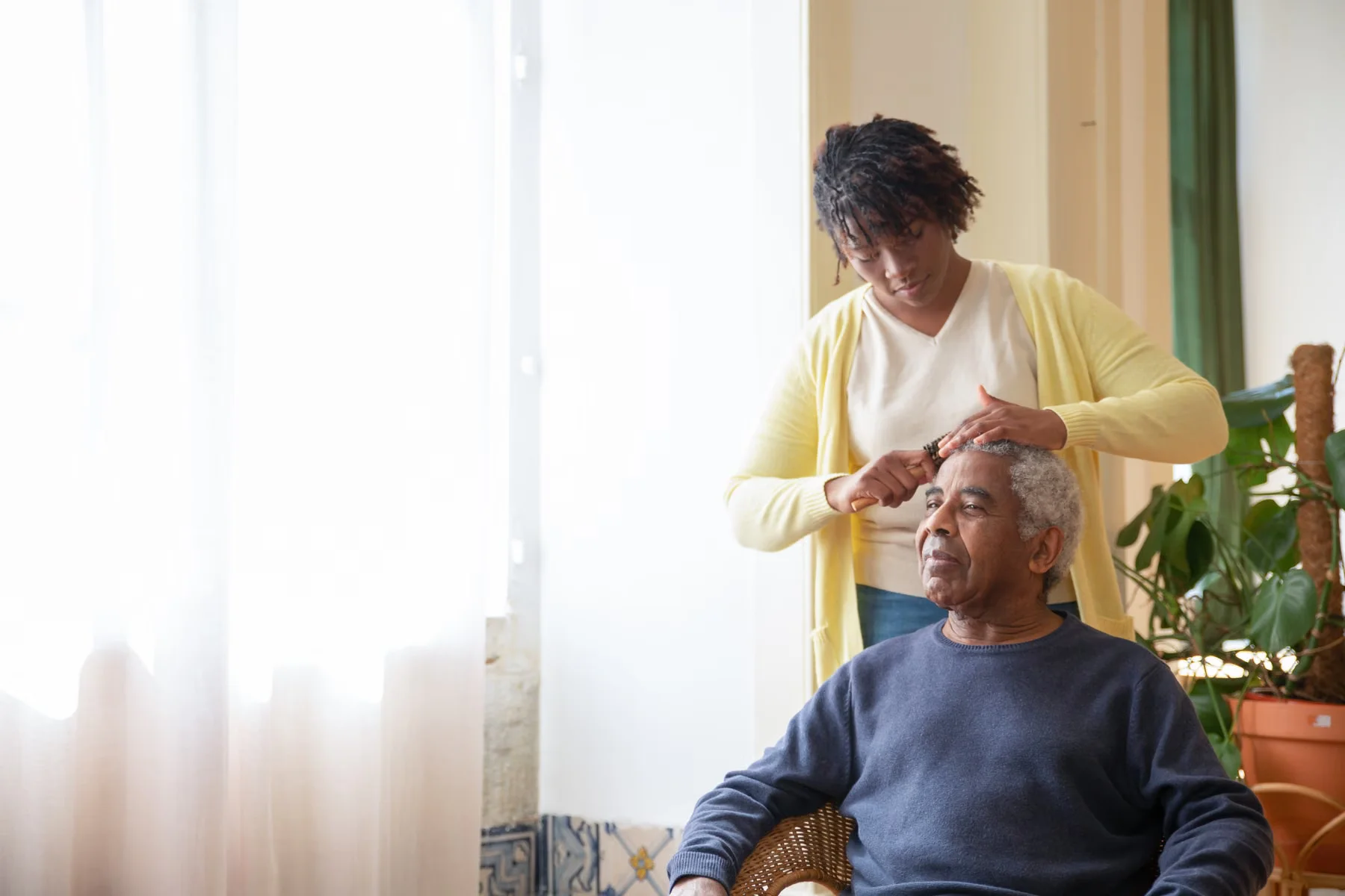 A caregiver gently helping an older man with his hair.
