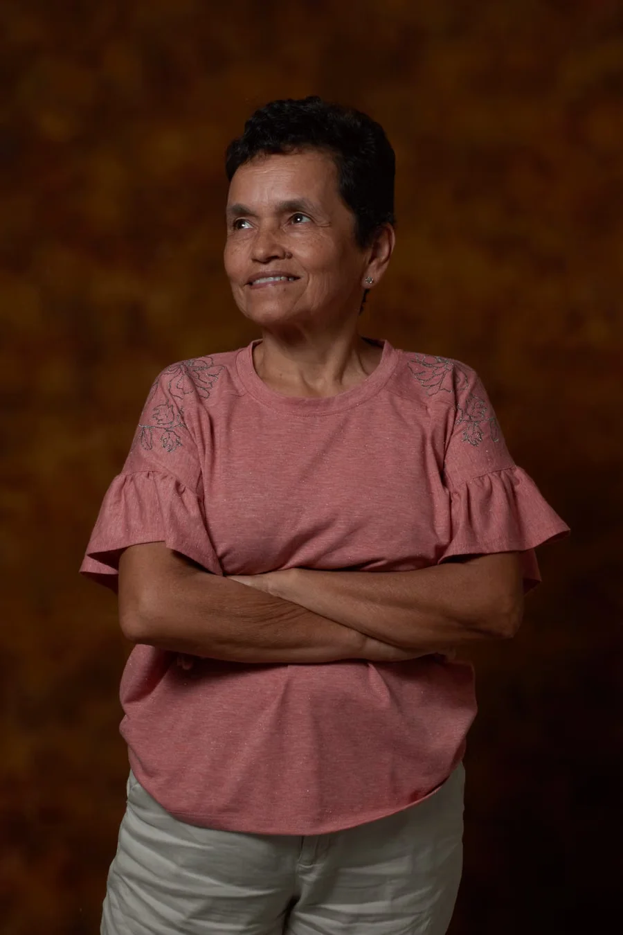An older woman standing with her arms folded and smiling.