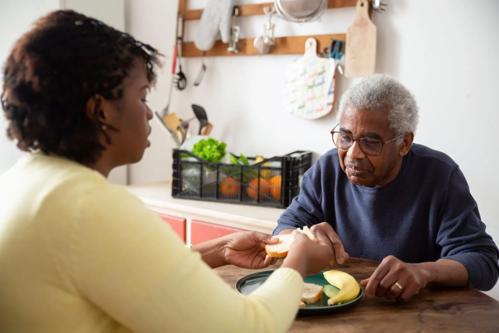 An older adult and a companion sharing time at a kitchen table.