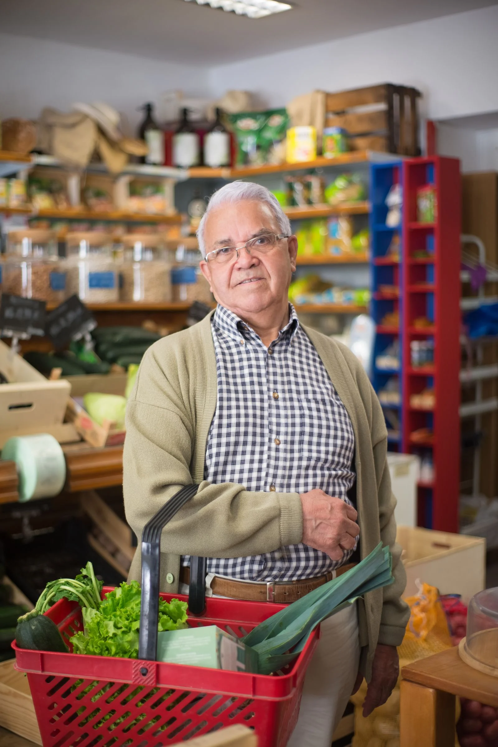 An older man shopping with a basket of vegetables.
